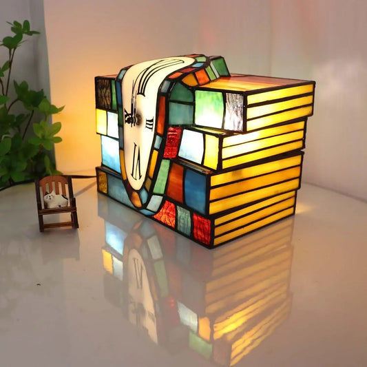 Tiffany stained glass melting clock lamp draped over a stack of books, accent table lamp for home decor.