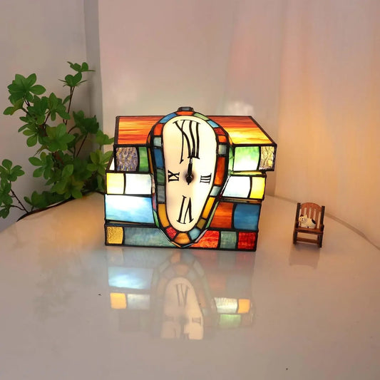 Tiffany stained glass melting clock lamp draped over stack of books accent table lamp illuminated on surface.